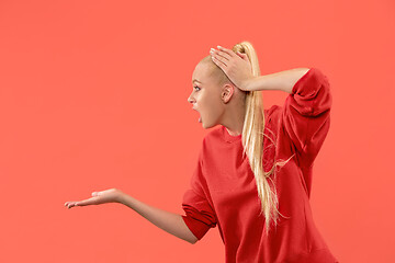 Image showing Beautiful female half-length portrait isolated on coral studio backgroud. The young emotional surprised woman