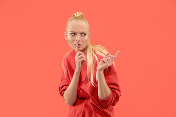 Image showing The young woman whispering a secret behind her hand over coral background