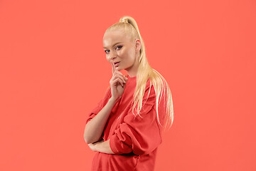 Image showing The young woman whispering a secret behind her hand over coral background