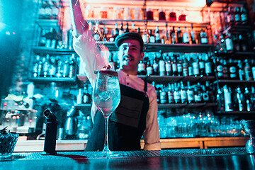 Image showing Glass of fiery cocktail on the bar counter against the background of bartenders hands with fire