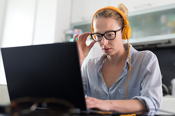 Image showing Female freelancer in her casual home clothing working remotly from her dining table in the morning. Home kitchen in the background.