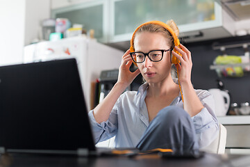 Image showing Female freelancer in her casual home clothing working remotly from her dining table in the morning. Home kitchen in the background.