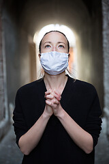 Image showing Coronavirus outbreak. Young caucasian woman wearing medical protection face mask praying over coronavirus global pandemic, for salvation of humanity, health, anxiety and depression reduction