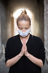 Image showing Coronavirus outbreak. Young caucasian woman wearing medical protection face mask praying over coronavirus global pandemic, for salvation of humanity, health, anxiety and depression reduction