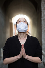 Image showing Coronavirus outbreak. Young caucasian woman wearing medical protection face mask praying over coronavirus global pandemic, for salvation of humanity, health, anxiety and depression reduction