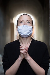 Image showing Coronavirus outbreak. Young caucasian woman wearing medical protection face mask praying over coronavirus global pandemic, for salvation of humanity, health, anxiety and depression reduction