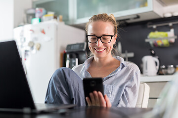 Image showing Stay at home and social distancing. Woman in her casual home clothing working remotly from kitchen dining table. Video chatting using social media with friend, family, business clients or partners