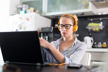 Image showing Female freelancer in her casual home clothing working remotly from her dining table in the morning. Home kitchen in the background.