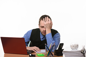 Image showing tired and exhausted office employee rests his head on his hand sitting at the table