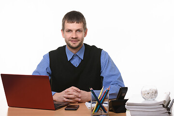 Image showing An office worker sits at a table clutching his fingers and looks into the frame