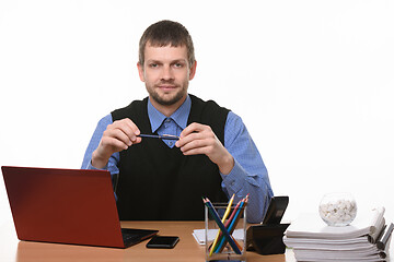 Image showing a man sits at an office table and holds a pen on a white background