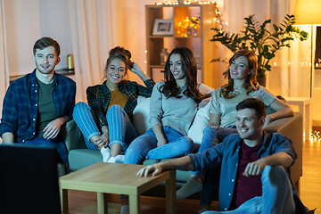 Image showing happy friends watching tv at home in evening