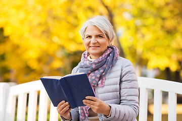 Image showing happy senior woman reading book at autumn park