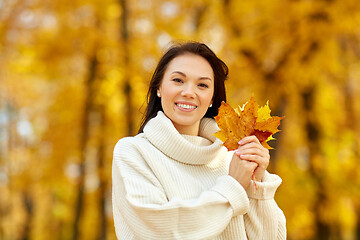 Image showing happy young woman with maple leaves in autumn park