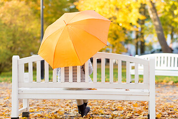 Image showing woman with umbrella sits on bench in autumn park