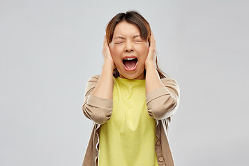 Image showing stressed asian woman closing ears and screaming