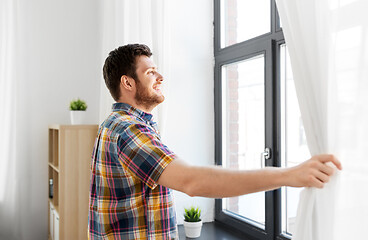 Image showing young man opening window curtain at home