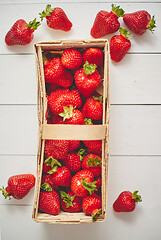 Image showing Wooden container with fresh red strawberries. Placed on white table.