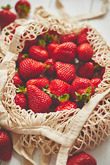 Image showing Fresh strawberries in eco-friendly package on white wooden background. Vegetarian organic meal