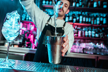 Image showing Expert barman is making cocktail at night club.