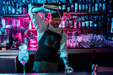 Image showing Expert barman is making cocktail at night club.