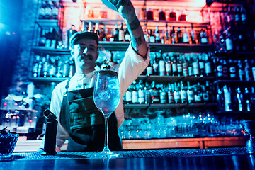 Image showing Glass of fiery cocktail on the bar counter against the background of bartenders hands with fire