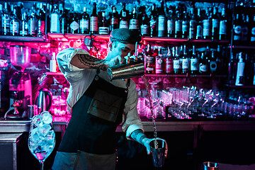 Image showing Expert barman is making cocktail at night club.