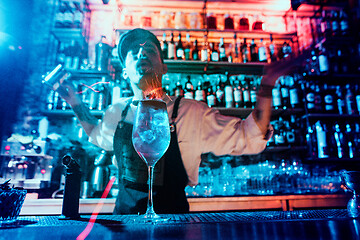 Image showing Glass of fiery cocktail on the bar counter against the background of bartenders hands with fire