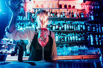 Image showing Glass of fiery cocktail on the bar counter against the background of bartenders hands with fire