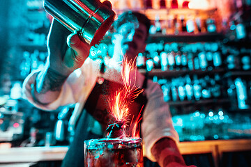 Image showing Glass of fiery cocktail on the bar counter against the background of bartenders hands with fire