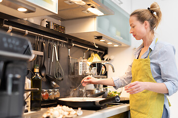 Image showing Stay at home housewife woman cooking in kitchen, salting dish in a saucepan, preparing food for family dinner.