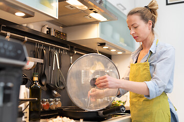 Image showing Stay at home housewife woman cooking in kitchen, stir frying dish in a saucepan, preparing food for family dinner.