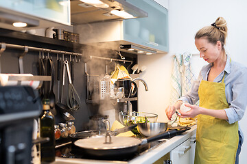 Image showing Stay at home housewife woman cooking in kitchen, salting dish in a saucepan, preparing food for family dinner.