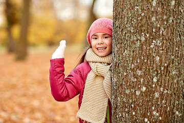 Image showing happy girl peeking out tree in autumn park