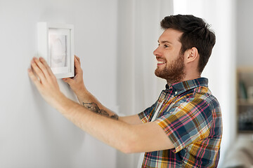 Image showing man hanging picture in frame to wall at home