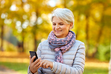 Image showing happy senior woman with smartphone at autumn park