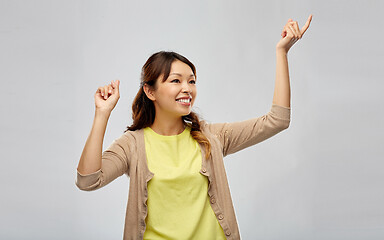 Image showing happy asian woman dancing over grey background