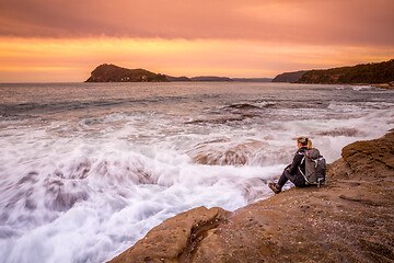 Image showing Woman sits by the ocean watching the waves flow back and forth