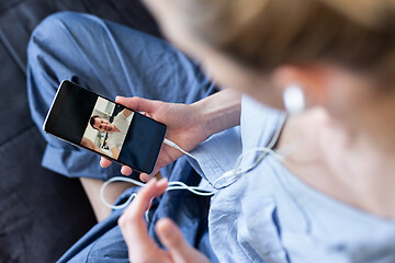 Image showing Woman at home relaxing on sofa couch using social media on phone for video chatting with her loved ones during corona virus pandemic. Stay at home, social distancing lifestyle.