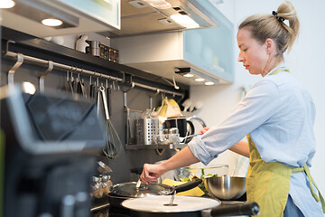 Image showing Stay at home housewife woman cooking in kitchen, stir frying dish in a saucepan, preparing food for family dinner.