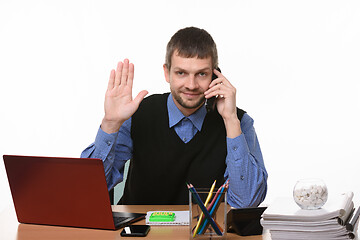 Image showing The man sitting at the table and talking on the phone raised his hand in greeting