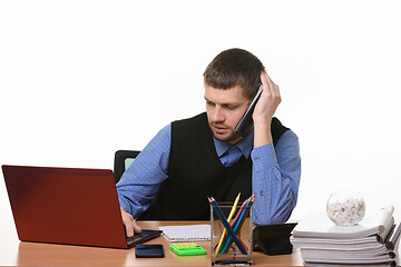 Image showing A tired employee negotiates on the phone looking into the screen of the laptop