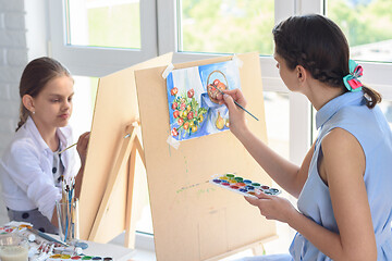 Image showing Mom and daughter spend leisure time at home painting on easels by the window