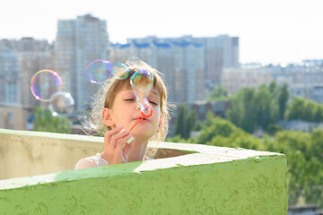 Image showing A child is having fun on the balcony of a multi-storey building blowing soap bubbles