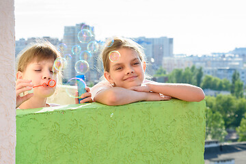 Image showing Two girls blow bubbles on the balcony of a multi-storey building