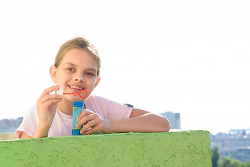 Image showing Happy girl on the balcony of a high-rise building stands with a jar of soap bubbles