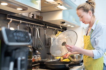 Image showing Stay at home housewife woman cooking in kitchen, stir frying dish in a saucepan, preparing food for family dinner.