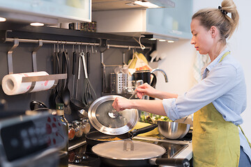 Image showing Stay at home housewife woman cooking in kitchen, stir frying dish in a saucepan, preparing food for family dinner.