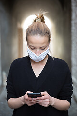 Image showing COVID-19 pandemic coronavirus. Casual caucasian woman at medieval city street using mobile phone, wearing protective face mask against spreading of coronavirus and disease transmission