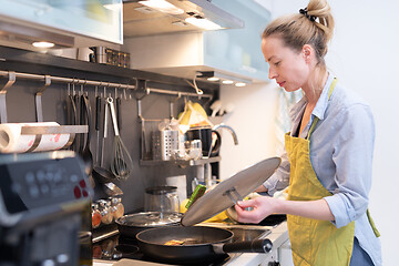 Image showing Stay at home housewife woman cooking in kitchen, stir frying dish in a saucepan, preparing food for family dinner.